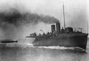 A torpedo boat, with steam pouring from a steam stack, fires a torpedo