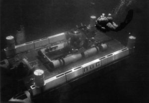 Black and white photograph of Makakai underwater sitting atop an underwater platform