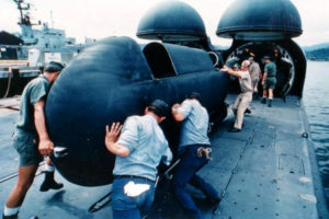 Sailors push a Mark 7 Mod 6 swimmer delivery vehicle on the deck of a submarine into a cylindrical deck chamber