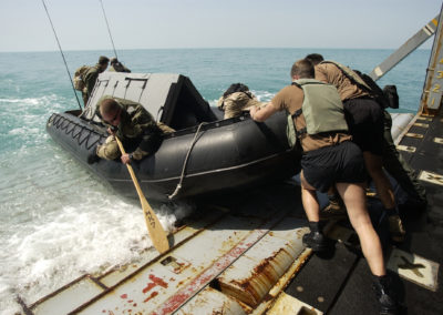 Sailors push a small boat containing a dolphin into the water.