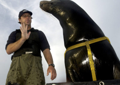 A man gives a hand signal command to a sea lion.