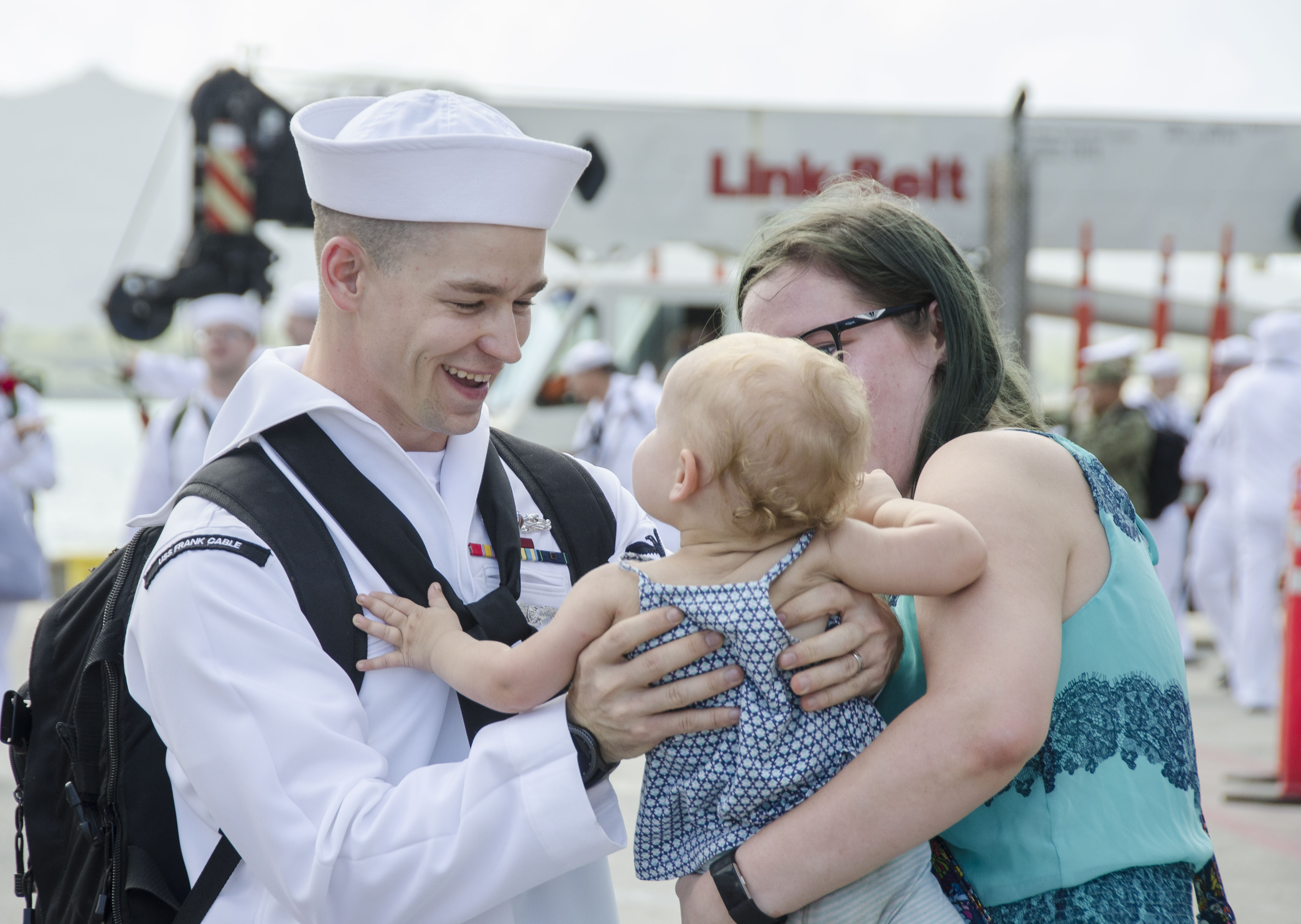 A sailor greets his partner and child at homecoming.