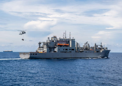 A large ship sails through the water as a helicopter approaches.