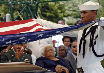 A Sailor holds two corners of outstretched American flag.