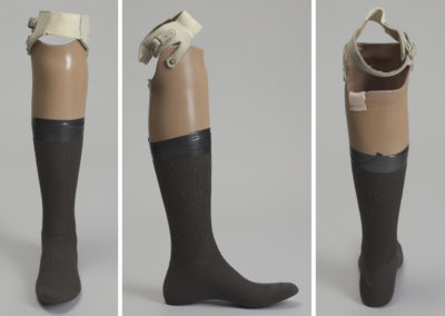 Three views of a prosthetic leg with light brown skin and a tall black sock taped to the calf.