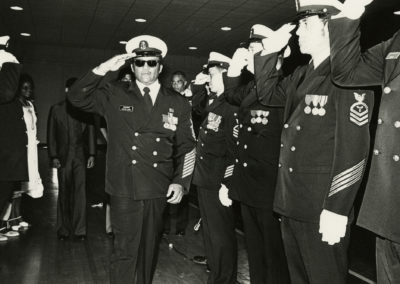Carl Brashear salutes as two lines of Sailors salute him.