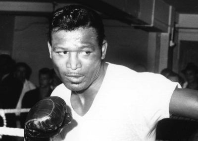 Sugar Ray Robinson winds up for a punch wearing boxing gloves.