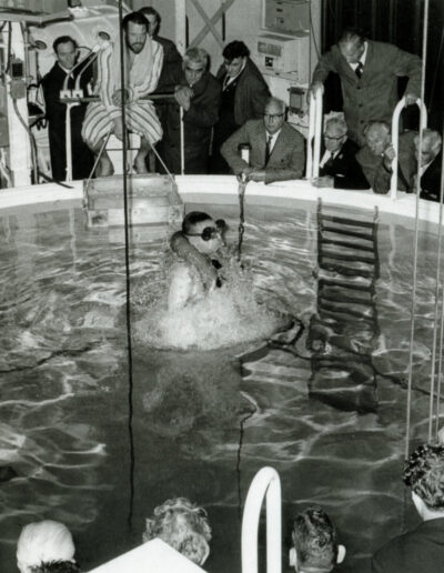 A man breaks the surface of a pool while several people watch.