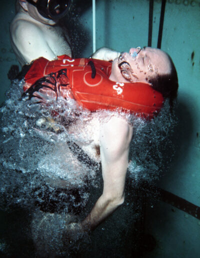 A man shoots upward through the water while wearing a red inflated vest.