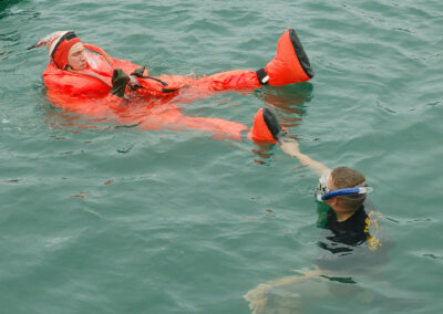 A submariner in a bright red-orange escape suit floats on the water's surface.