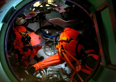 Bright red-orange escape suits sit inside a cylindrical chamber.