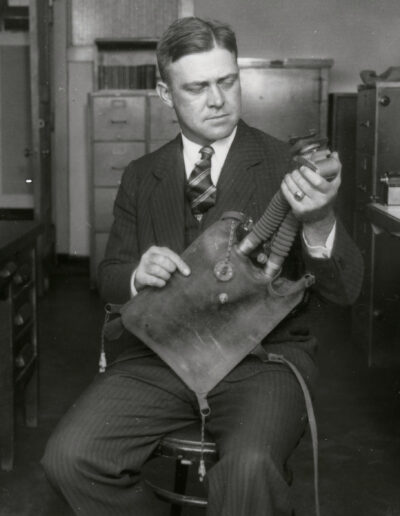A man in a suit holds a rectangular-shaped bag with hoses.