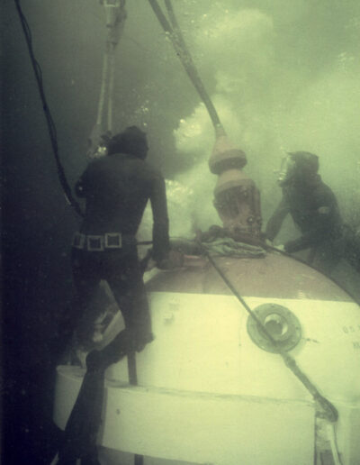 Divers grasp at cables attached to a white and red sphere.