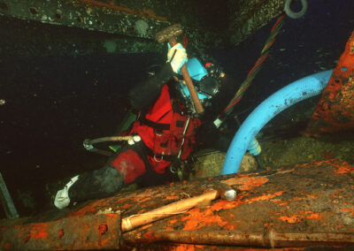 A diver hammers a chisel into a rusty metal structure while underwater.