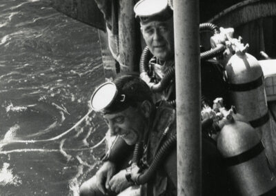 Two men wear SCUBA gear as they prepare to enter the water.