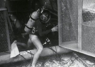 A diver wearing SCUBA gear climbs into a cage around the Sealab habitat.