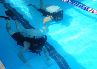 Two Explosive Ordnance Disposal divers wear Mark 16 rebreathers on their backs while swimming in a pool.