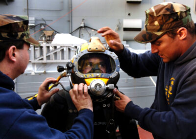 Two diving tenders adjust the helmet on a waiting diver.