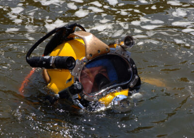 A diver wears a yellow Mark 21 diving helmet as his head breaks above the water.