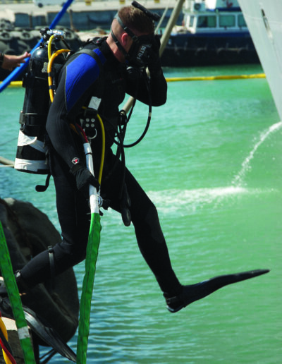 A diver jumps into the water wearing a wet suit, face mask, and oxygen tank.