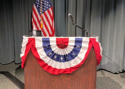 Lectern on Auditorium stage with red, white, and blue bunting wrap. U.S. flag in background.