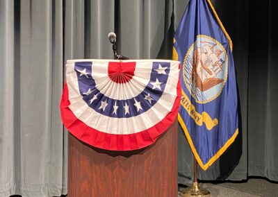 Lectern on Auditorium stage with red, white, and blue bunting wrap. U.S. Navy flag in background.