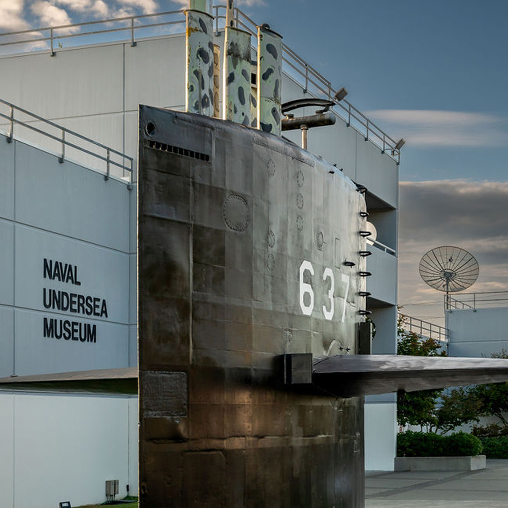 A red-orange remotely operated vehicle is lowered into the water. Decals with eyes and pointy teeth are attached to the front of the vehicle.