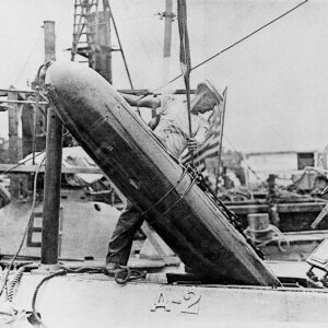 Early 1900s photo of a Sailor loading a Whitehead torpedo into a tiny submarine hatch